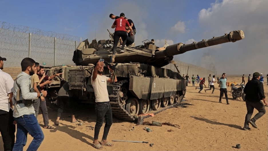 Palestinians take control of an Israeli tank after crossing the border fence with Israel from Khan Younis in southern Gaza on 7 October 2023 (Said Khatib/AFP)